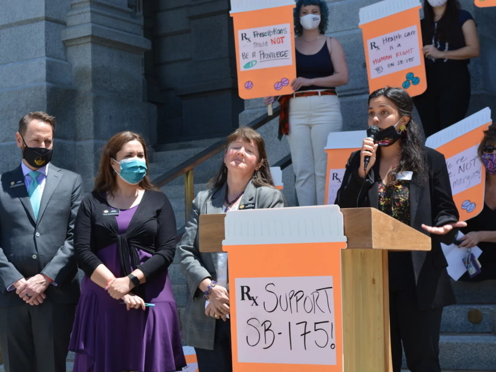 People stand at a podium with signs of support for SB 175.