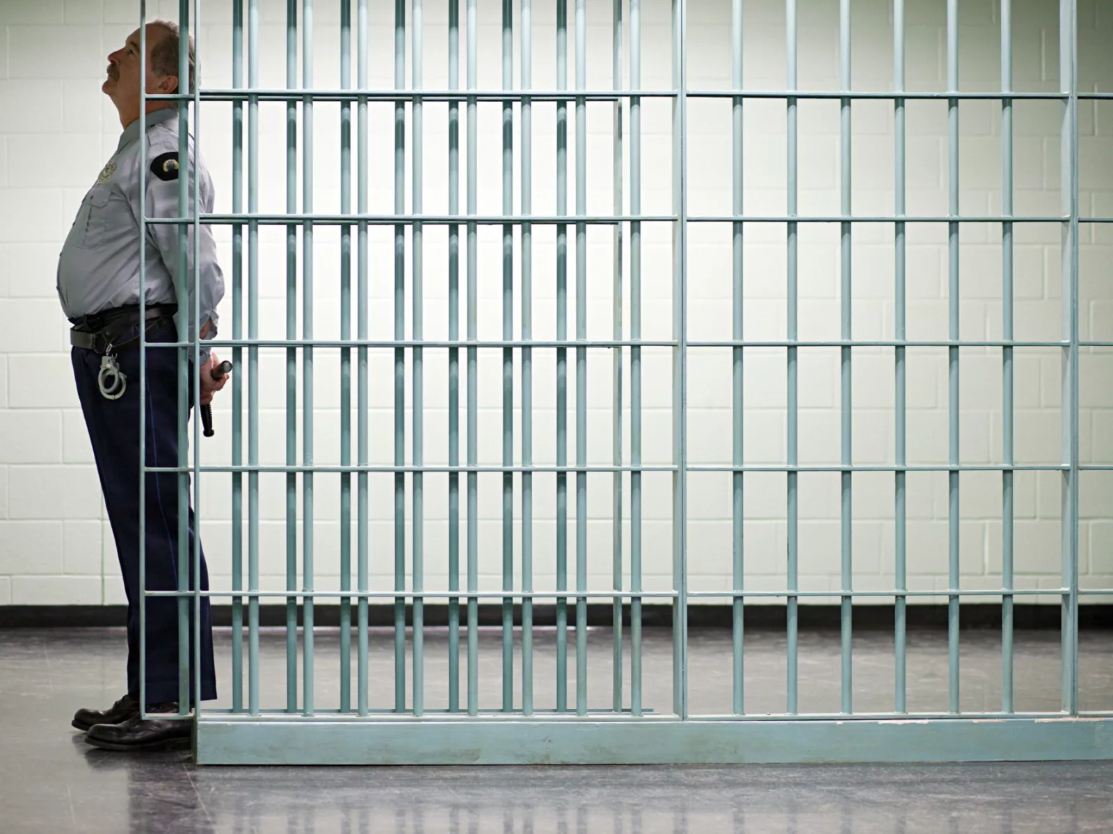 Image of male guard standing along the side of a jail cell.