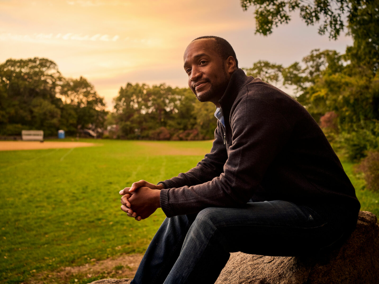Rich Pierre sitting in a field with sunset in the background.