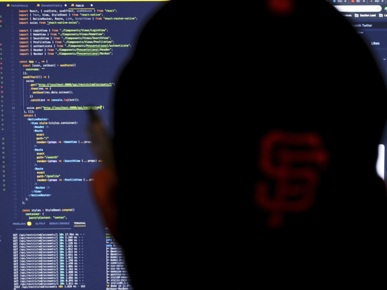 A man's profile is seen in front of a computer screen that shows computer coding entries.