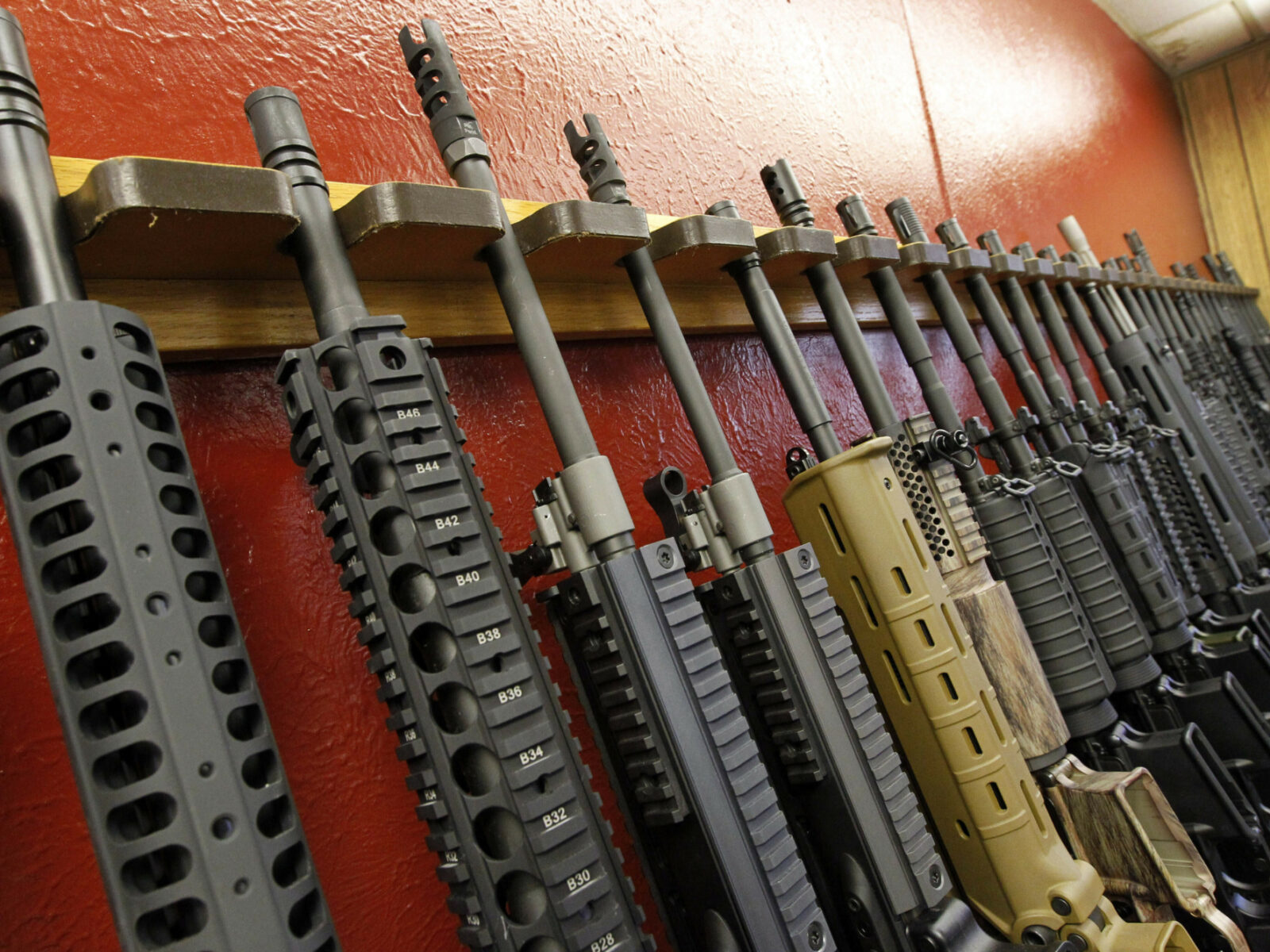 Guns are lined up against a brightly colored wall.