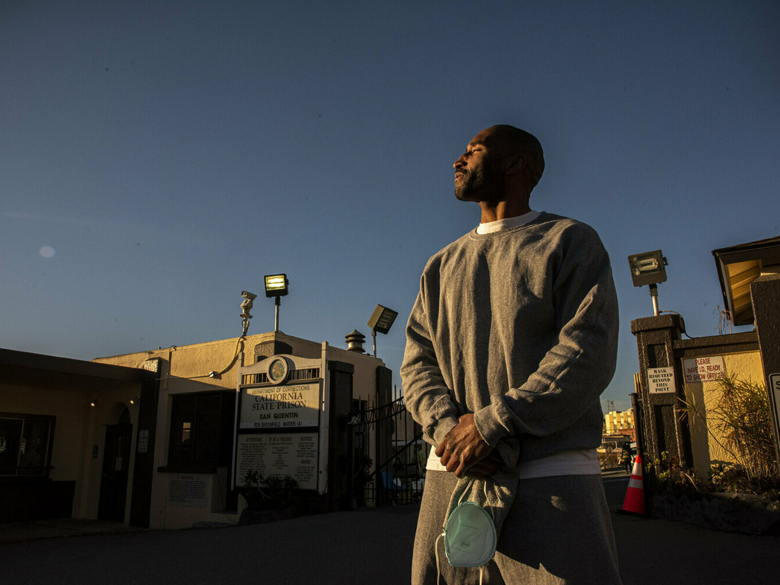 Kennard Love standing with hands clasped and looking to the left outside San Quentin prison with sunlight reflecting om his face.