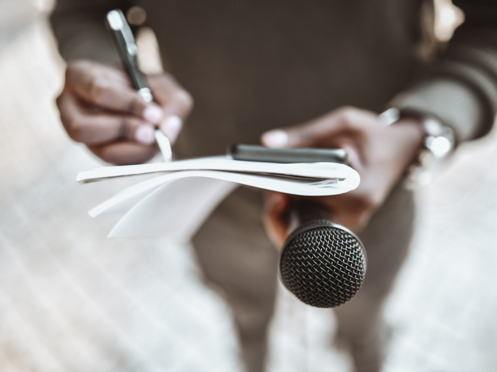 Reporter holds pen, notebook and microphone while taking notes.