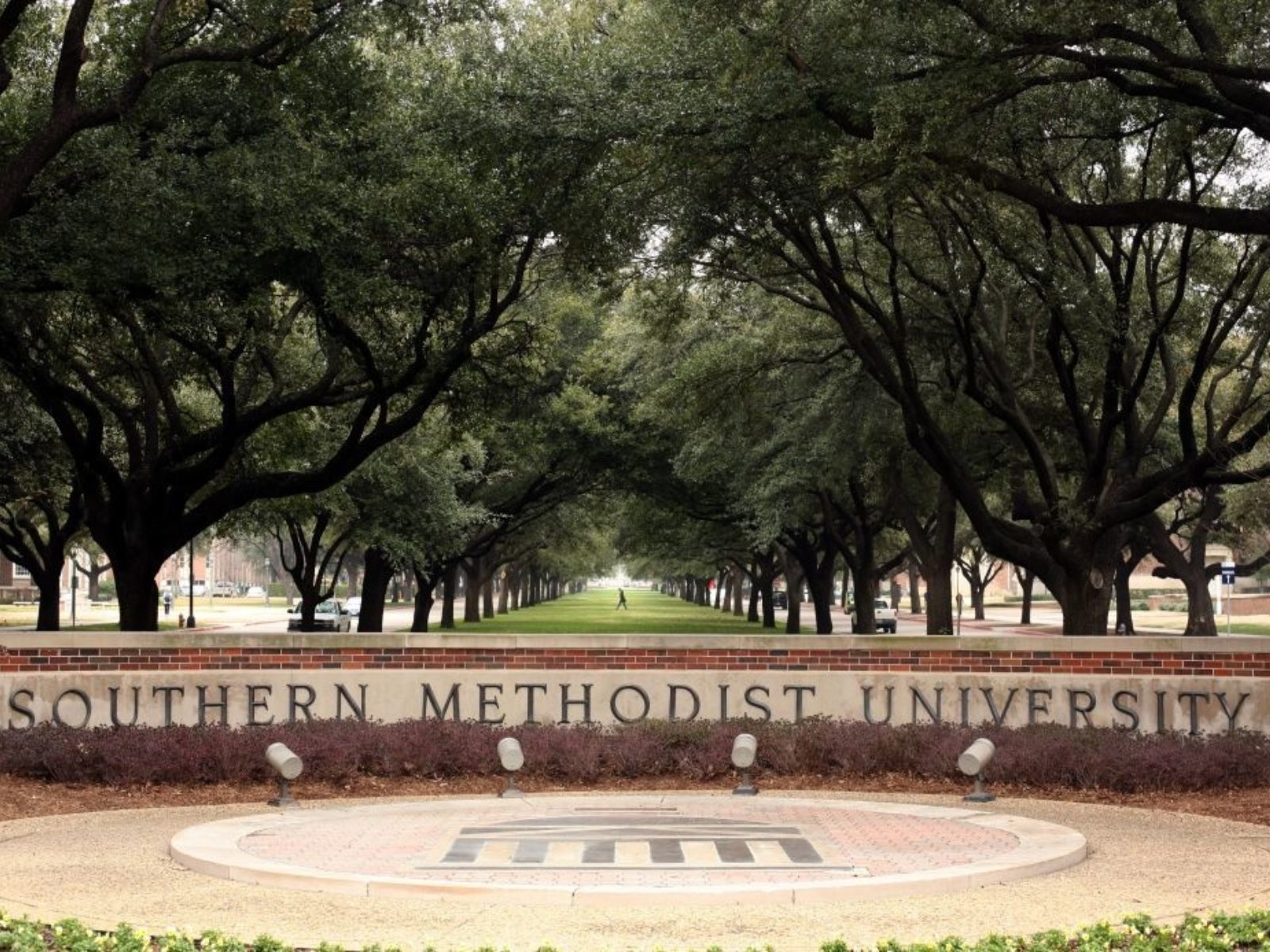 A sign for Southern Methodist University is sen on campus with large trees in the background.