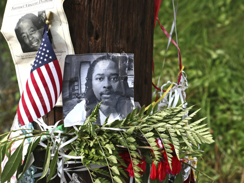 An printed image of Samuel DuBose is attached to a tree surrounded by flowers.