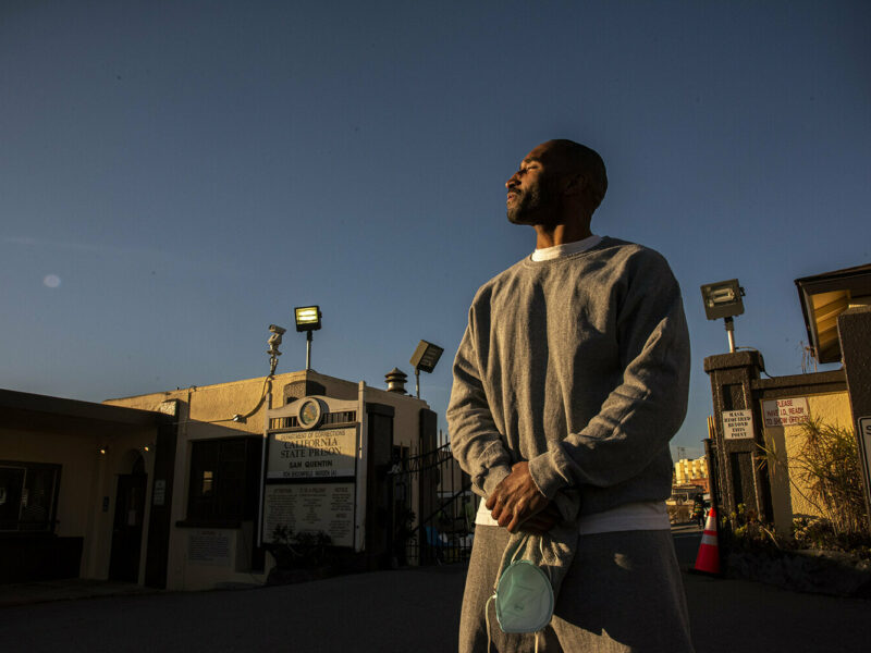 Kennard Love standing with hands clasped and looking to the left outside San Quentin prison with sunlight reflecting om his face.